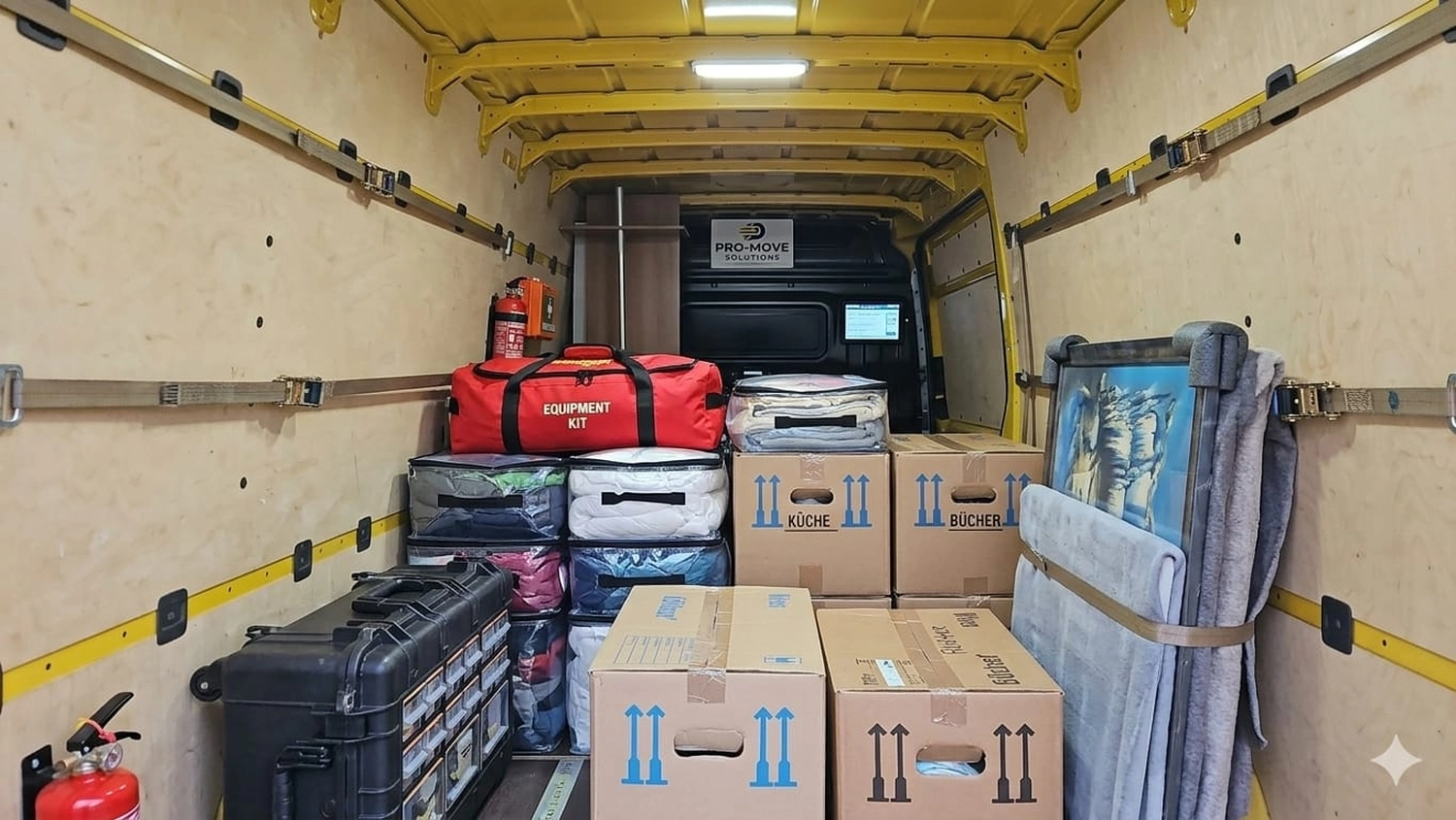 ET Transporte & Express - Der Innenraum eines Lieferwagens ist mit verschiedenen Gütern gefüllt, darunter eine rote Ausrüstungstasche, gestapelte Kartons und in blaues Schutzmaterial eingewickelte Gegenstände. Der Laderaum wird gut genutzt.